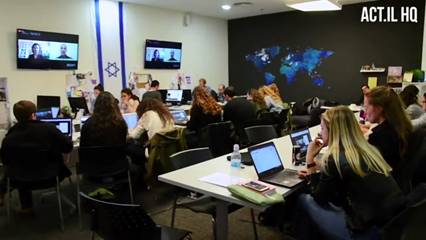 People in a room sit at computers with an Israeli flag on the wall
