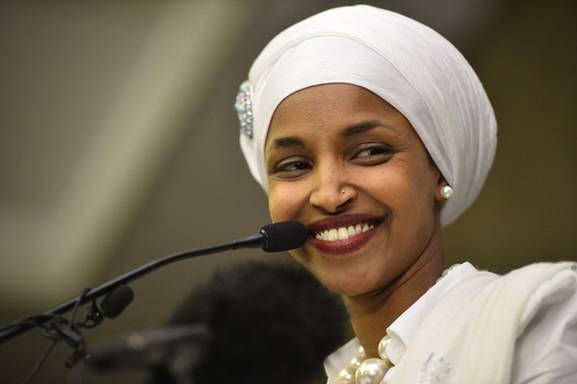 Ilhan Omar smiles in front of a microphone.