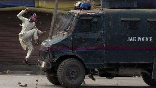A masked Kashmiri protester jumps on the bonnet of an armoured vehicle of Indian police as he throws stones at it during a protest in Srinagar [Dar Yasin/AP]